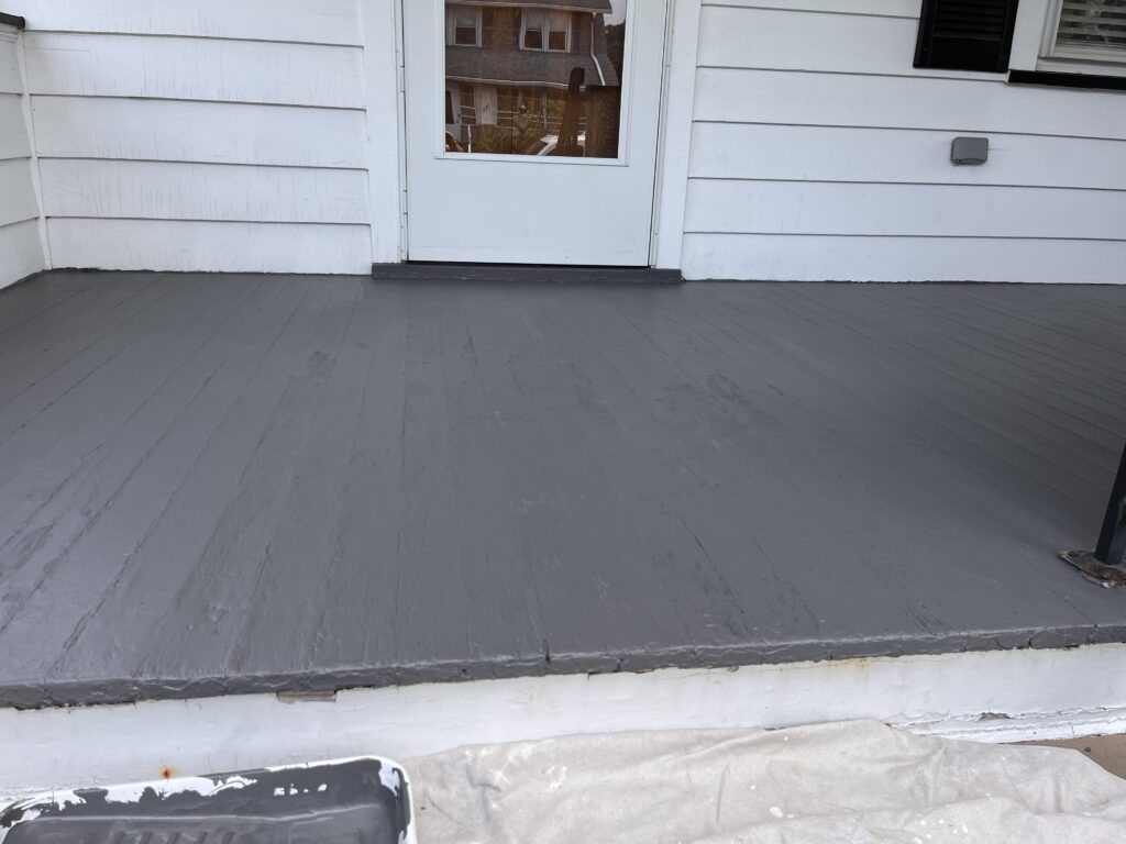 Freshly painted gray front porch with white siding and a white door.